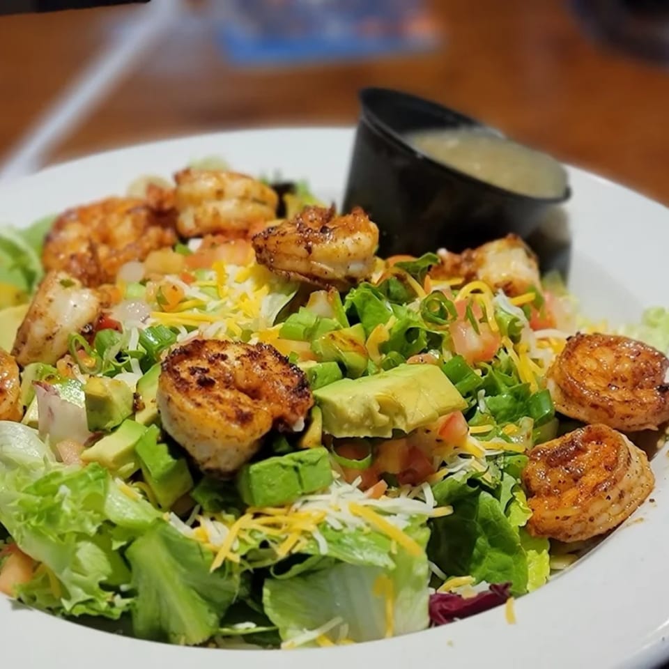 A close-up of a shrimp salad with avocado, cheese, and dressing on a white plate.