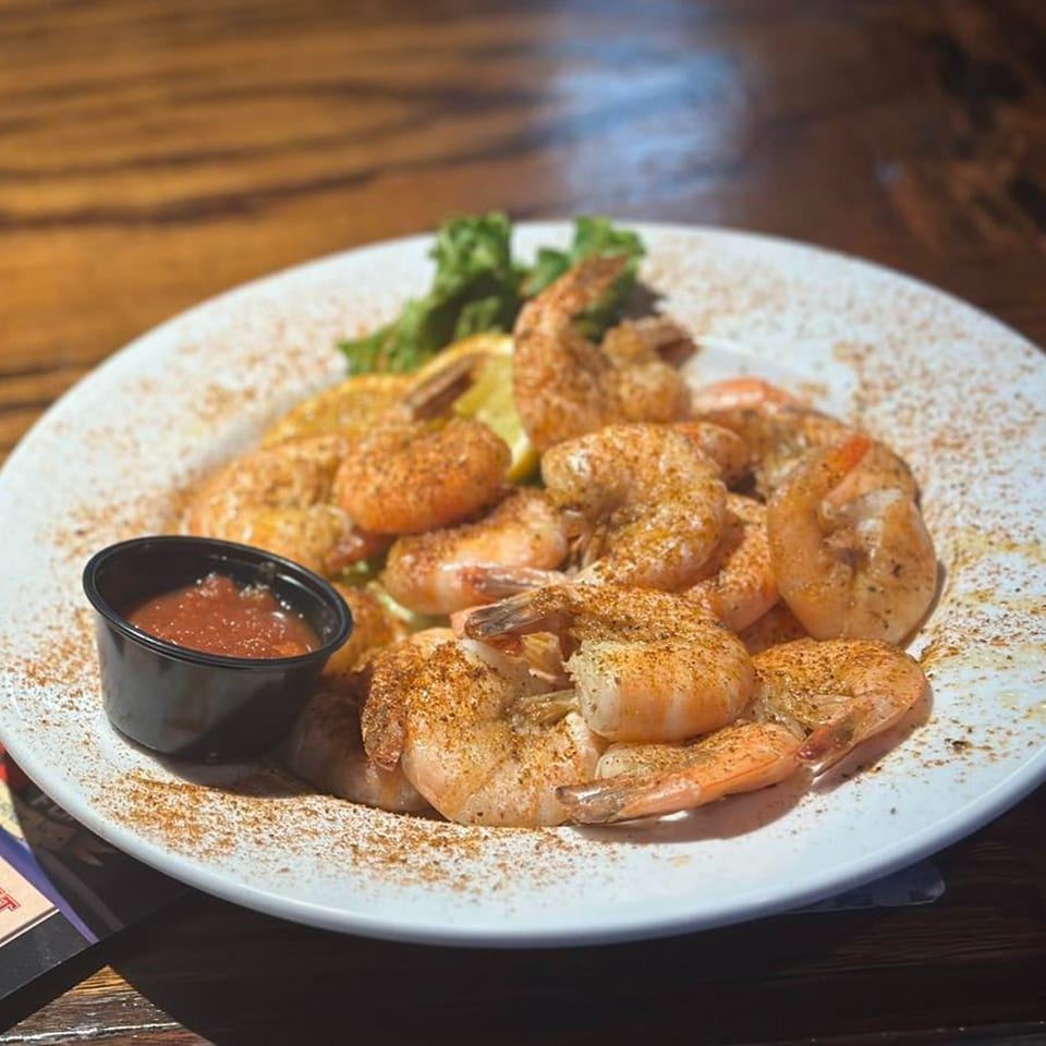 A plate of seasoned shrimp with lemon wedges, lettuce, and a side of cocktail sauce.