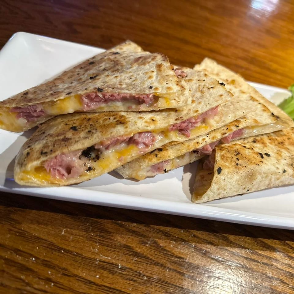 Triangular quesadilla slices filled with melted cheese and meat, served on a white rectangular plate.