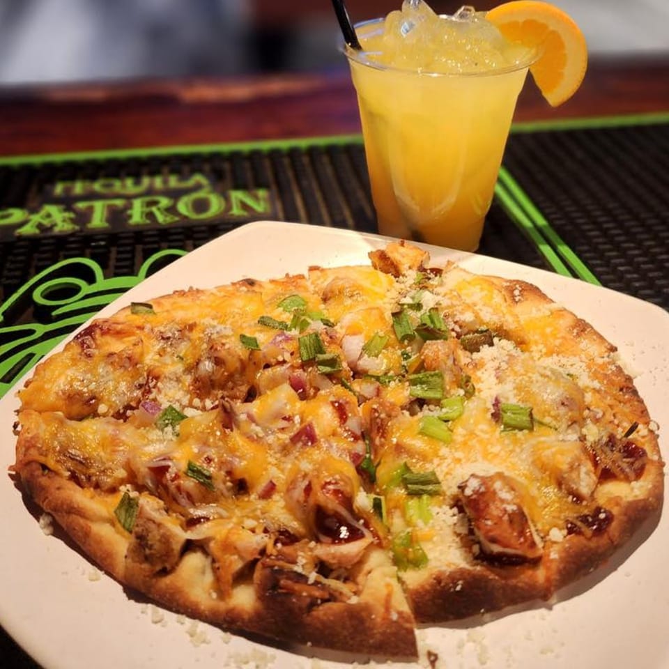 BBQ chicken flatbread with melted cheese, green onions, and a bright orange cocktail.